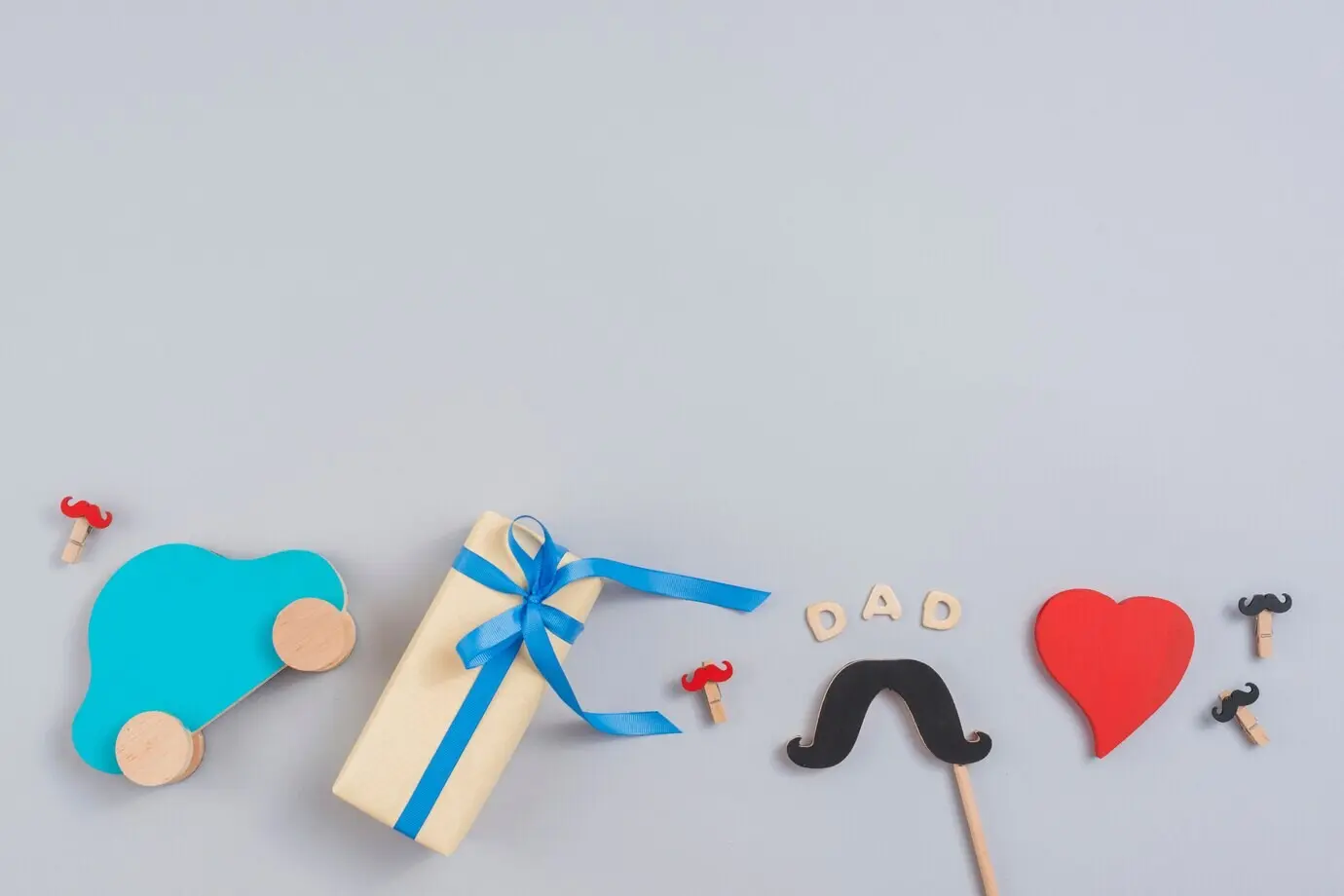 Schriftzug 'Dad' mit Geschenkbox, Spielzeugauto und Papierschnurrbart